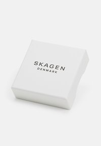 Caja rectangular blanca con acabado mate, con "SKAGEN DENMARK" impreso en negro en la parte superior, vista en ángulo que muestra el lado.