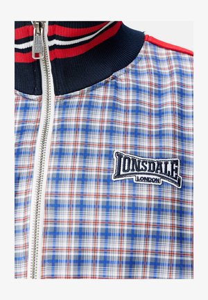 Kostkovaná bunda s modrými, červenými a bílými vzory a námořnickým límcem. Přední zip, vyšívané logo "Lonsdale London" na hrudi.