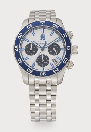 Montre chronographe avec un bracelet en acier inoxydable, un cadran blanc, une lunette bleue et des accents bleus. Comprend trois sous-cadrans et une fenêtre de date.
