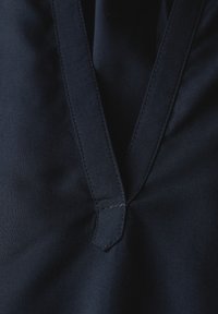 Tessuto blu navy con una superficie liscia; presenta un colletto a V e cuciture in contrasto lungo i bordi.