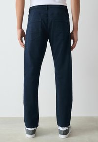 Pantaloni dritti color blu marina scuro con due tasche posteriori, dettagli di cuciture visibili e leggera scoloritura. Indossati con sneaker grigie e bianche.