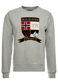Sudadera gris de mezcla de algodón, con un logo de escudo colorido que incluye texto, ejes cruzados y un diseño de montaña en la parte frontal.