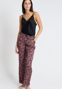 Czarna satynowa koszulka na ramiączkach z koronkowym wykończeniem w połączeniu z różowymi spodniami w kwiatowy wzór, z kieszeniami i luźnym krojem.