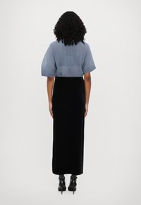 Himmelbluse mit Falten und kurzen Ärmeln, kombiniert mit einem schwarzen langen Rock, der eine glatte Textur, eine taillierte Passform und knöchelhohe schwarze Stiefel aufweist.