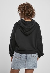 Sudadera negra con capucha y mangas raglán, combinada con una mini falda de mezclilla azul clara con dobladillo deshilachado y bolsillos traseros.