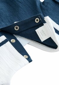 Marineblauwe en witte baby-outfit met drukknoopsluitingen. Zachte textuur, label zichtbaar; modern ontwerp met contrasterende kleuren en subtiele stiksels.