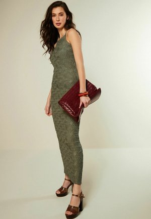 Olivgrön figursydd klänning med texturerat mönster, kombinerad med bruna platåsandaler och en vinröd vävd clutch.