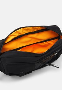 Black fabric bag with a zippered opening, featuring an orange lining and multiple interior compartments for organization.