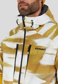 Gul og hvid mønstret jakke med høj krave, justerbar hætte og sorte lynlåse, med to forlommer foran og logodetalje.