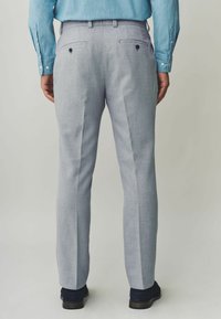 Pantaloni grigi sartoriali in tessuto strutturato, con due tasche posteriori con bottoni e taglio dritto. Indossati con una camicia azzurro chiaro.