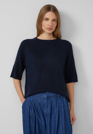 Maglione a maglia blu navy con maniche corte e scollatura tonda. Texture morbida e vestibilità rilassata, abbinato a pantaloni in denim +leggeri blu chiaro a pieghe.