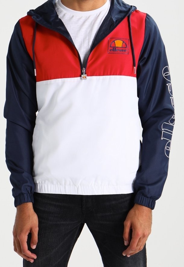 Nylon vindjacka med huva; har en röd övre del, vit midja, marinblå ärmar och logotyp på bröstet. Elastisk nederkant och ärmslut.