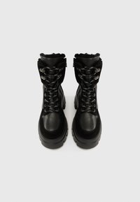 Botas de couro preto com acabamento texturizado, com ferragens prateadas, atacadores grossos e uma gola almofadada para maior conforto.