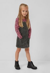 Zwarte denim overall jurk met zijzakken, gecombineerd met een roze lange mouwen shirt met een bloemenpatroon, en zwarte kniehoge laarzen.