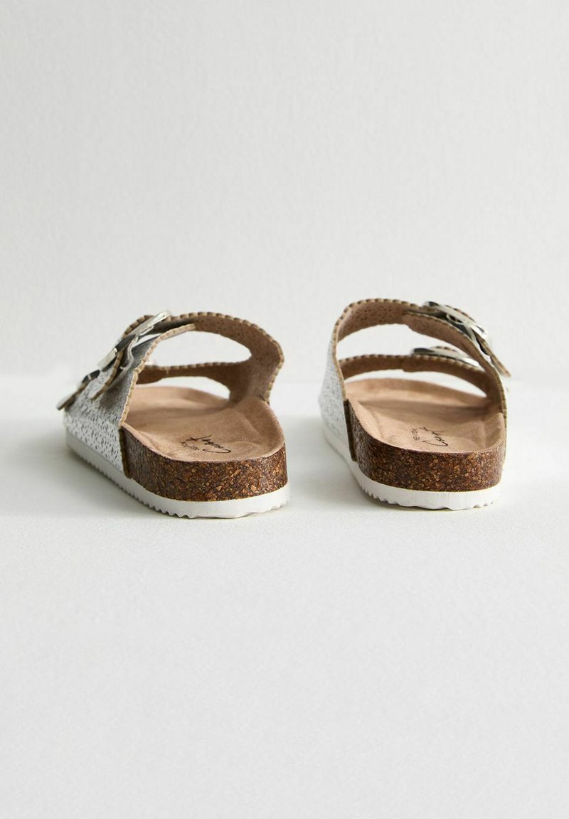 Srebrne, teksturowane sandały z korkową podeszwą i białą gumową podeszwą zewnętrzną. Posiada regulowane paski z metalowymi elementami, zapewniające pewne dopasowanie.
