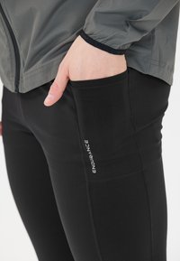 Svarta träningsbyxor med en sidoficka där ordet "ENDURANCE" är tryckt. I kombination med en grå, lätt zip-up jacka.