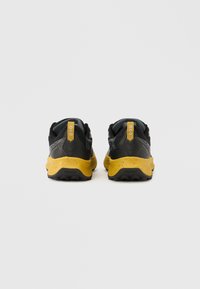 Sapatos de trail preto e amarelo com parte superior em tecido texturizado, sola amarela marcante e detalhes cinzentos contrastantes. Apresenta a marca Vibram na sola.