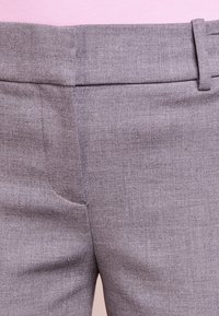 Pantalon en tissu gris avec une texture lisse, coupe ajustée, passants pour ceinture, et un détail de poche avant inclinée.