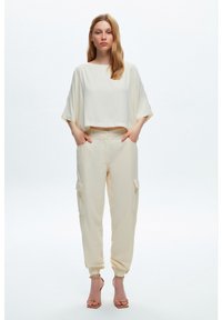 Crèmekleurig cropped top met brede mouwen en beige cargobroek met zakken, taps toelopende manchetten en een relaxte pasvorm. Draag met tan hakken.