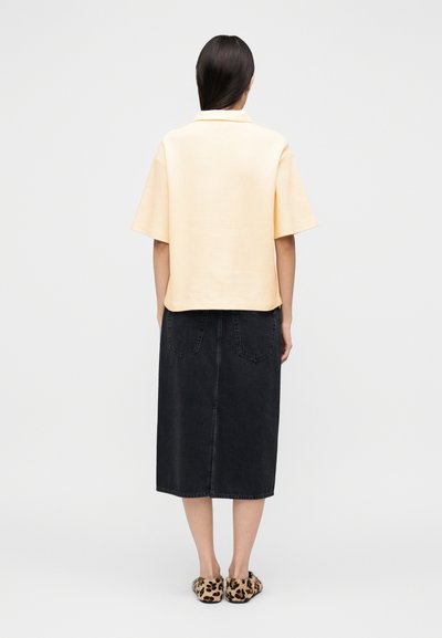 Ανοιχτό κίτρινο τοπ με κοντό μανίκι συνδυασμένο με μαύρη midi φούστα από τζιν και slip-ons με λεοπάρ σχέδιο, παρουσιάζοντας μια casual, άνετη γραμμή.