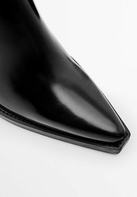 Black pointed-toe ankle boot made of shiny leather, featuring a sleek design, minimal stitching, and a flat, structured sole.