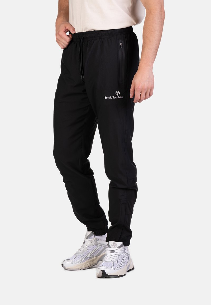 Zwarte sportbroek met elastische tailleband, zijzakken met rits en logo-detail. Glad materiaal met een getailleerde pasvorm en elastische boorden bij de enkels.