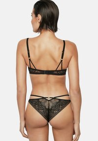 Ensemble de lingerie en dentelle noire comprenant un soutien-gorge à bretelles ajustables et un string assorti avec des motifs floraux délicats et des bords festonnés.