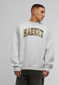 Szürke pulóver hosszú ujjal, hangsúlyos "MARKET" felirattal, álcázó mintával. Kerek nyakú és laza szabású, bordás mandzsettákkal.