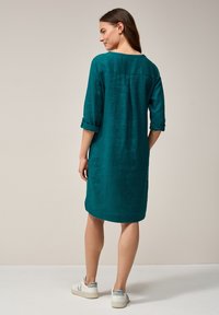 Turkoosi pellavamekko, jossa on kolme neljäsosaa hihat, hieman polven ylle ulottuva pituus, jossa on käänteet hihansuissa ja sivurei'ät, yhdistettynä valkoisiin tennareihin.