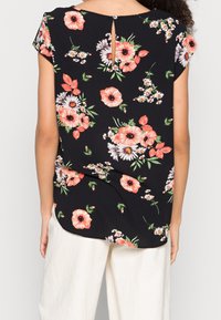 Blusa floral de tela negra con flores rosa y blancas. Mangas cortas y un pequeño detalle de ojal en la parte posterior. Dobladillo redondeado.