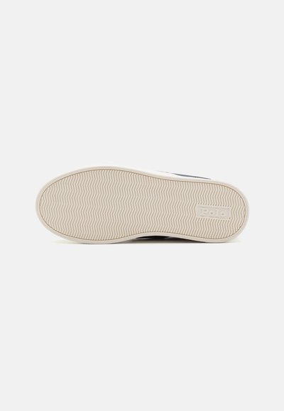 La suela del zapato presenta una superficie de goma texturizada con un patrón de espiga. El color es beige con una entresuela blanca y un sutil logotipo.