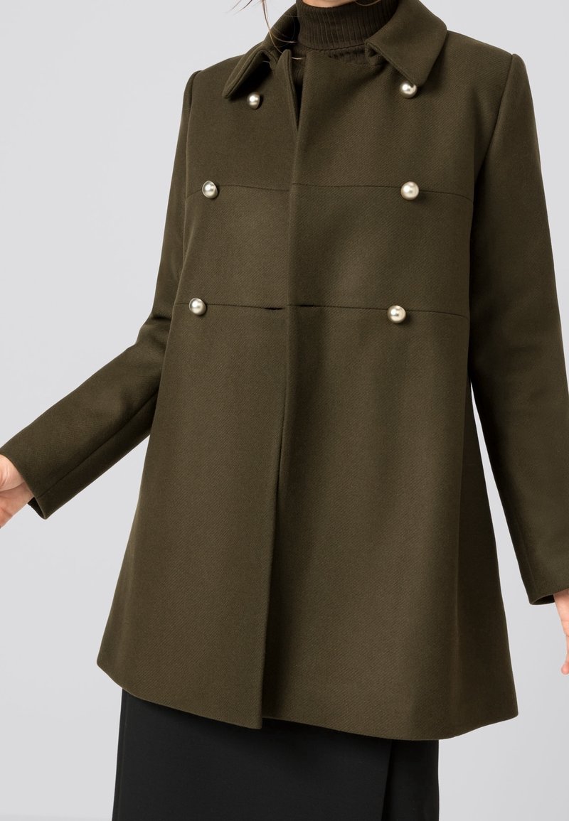 Olivgrön dubbelknäppt kappa med krage, strukturerad tyg och runda pärl-liknande knappar fram och vid ärmsluten.