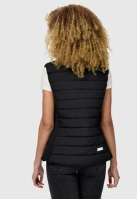 Gilet matelassé noir avec un design à coutures horizontales, matériau léger, col montant, fentes latérales et une petite étiquette au dos.