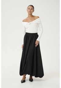 Bijela rebrovana majica s off-shoulder kragnom i čvorastim detaljem, u kombinaciji s lepršavom crnom maxi suknjom. Oba komada imaju ležeran kroj i glatku teksturu.