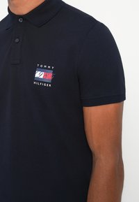 Mørkeblå polo skjorte laget av bomull, med en liten logo med røde, hvite og blå aksenter på venstre bryst og en klassisk passform.