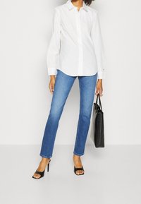 Vit skjorta med långa ärmar och en ficka; kombinerad med blå raka jeans, svarta kilklackar och en strukturerad svart handväska.