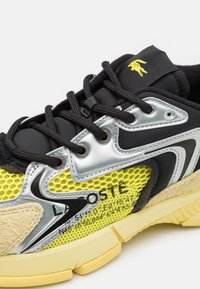 Baskets Lacoste avec une tige en mesh noir, un panneau en mesh texturé jaune, des accents argentés et du daim beige. Semelle épaisse en caoutchouc avec détails antidérapants.