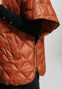 Kurtka pikowana w kolorze rdzy z zamkiem błyskawicznym i kieszenią boczną. Posiada czarny ściągacz na mankietach oraz gładką fakturę. Zaokrąglony dół.