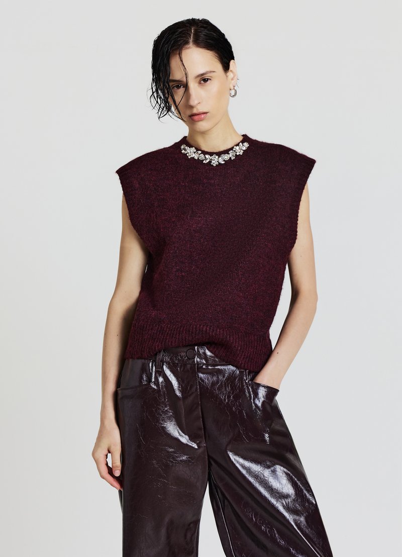 Burgundy sleeveless knit sweater with a textured finish and jeweled neckline, paired with shiny dark brown leather trousers.