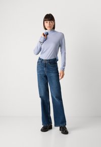 Light blue turtleneck sweater, fitted, paired with wide-leg dark blue jeans. Model holds a light blue accessory. Black platform shoes complete the look.