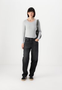 Light gray ribbed long-sleeve top paired with loose-fit black denim jeans. Model wears black sneakers with a gum sole. Additional black bag.