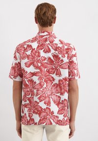 Korte mouw shirt gemaakt van witte stof met een rood bloemenpatroon, met grote, opvallende bloemen en een knoopsluiting kraagontwerp.