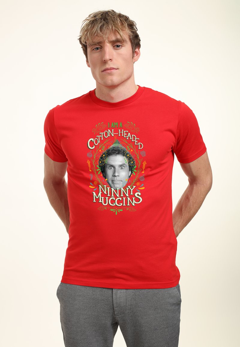 Młody mężczyzna o blond włosach, ubrany w czerwony T-shirt z czarno-białą twarzą i napisem "Jestem bawełnianą głupią gębą" w kolorowym wzorze.