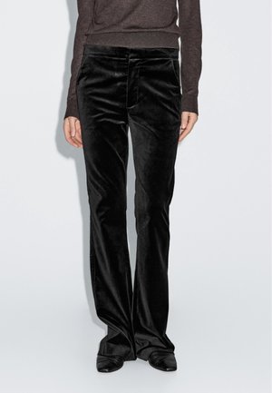 Person wearing black velvet straight-leg pants and black shoes, standing against a plain light background.