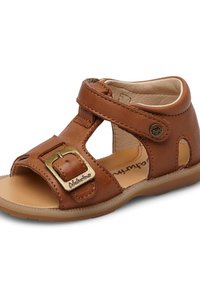 Brązowe skórzane sandały z regulowanym paskiem, detalem z klamrą, otwartymi bokami i płaską gumową podeszwą. Wnętrze wykończone beżowym materiałem.