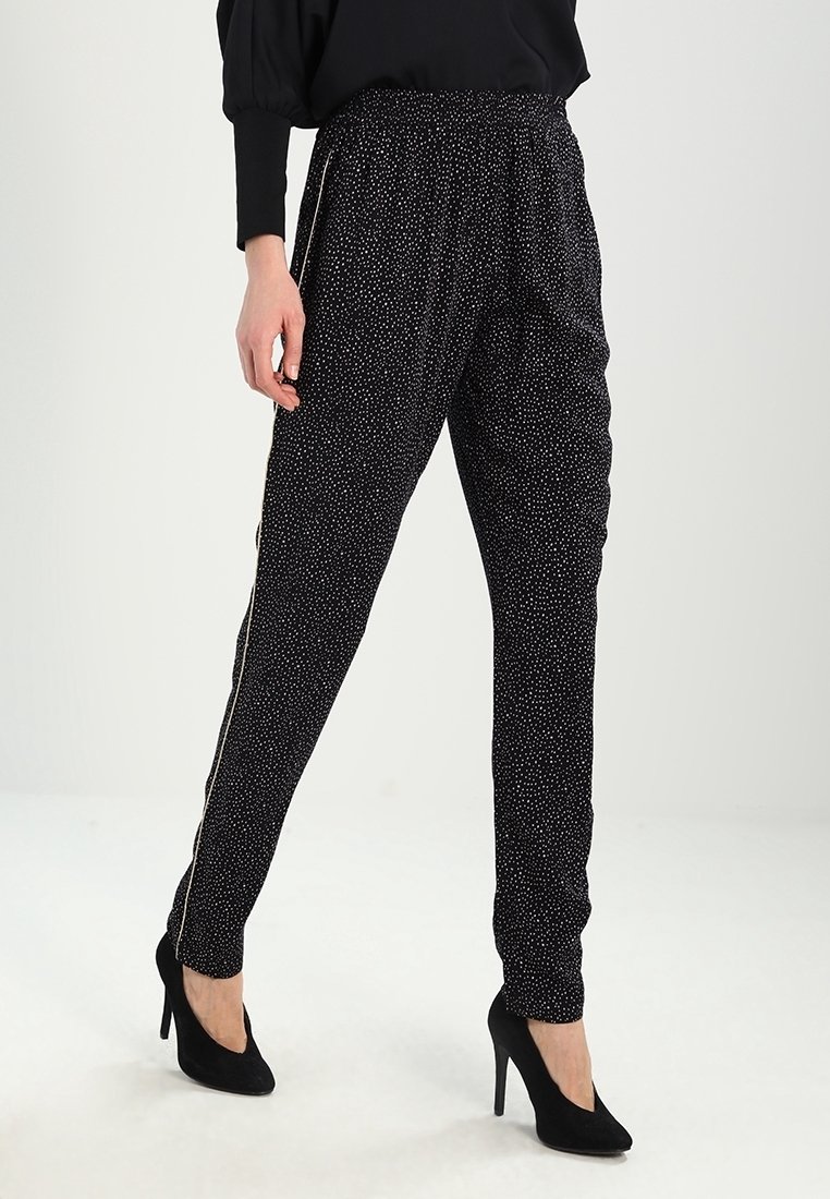 Czarne dresowe spodnie z elastycznym pasem i bocznymi paskami, ozdobione małymi białymi kropkami i zwężającym się krojem. W połączeniu z szpilkami.