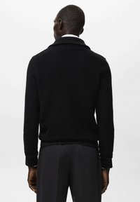 Czarny dziergany sweter z kołnierzem szalowym, fakturowanym materiałem i długimi rękawami, w połączeniu z dopasowanymi spodniami, widziany od tyłu.