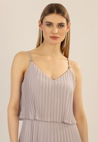 Helllila plissiertes Kleid mit V-Ausschnitt, dünnen Trägern, die mit silbernen Akzenten verziert sind, und einer fließenden Silhouette.