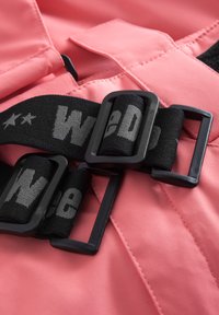 Rosa tyg med quiltad yta, utrustad med ett justerbart svart band med grå text och spännen, vilket betonar säker fastsättning.