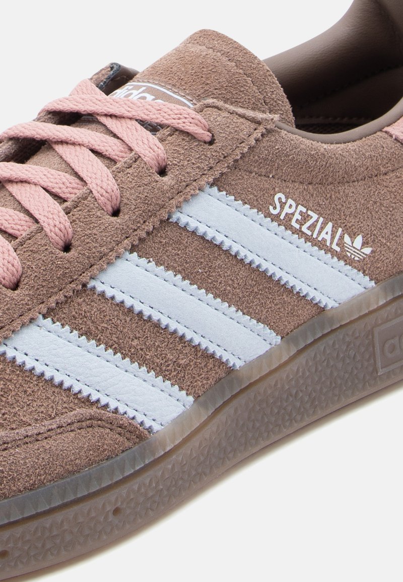 Baskets en daim marron avec trois bandes bleu clair, lacets roses et logo embossé. Semelle en caoutchouc transparent texturée.